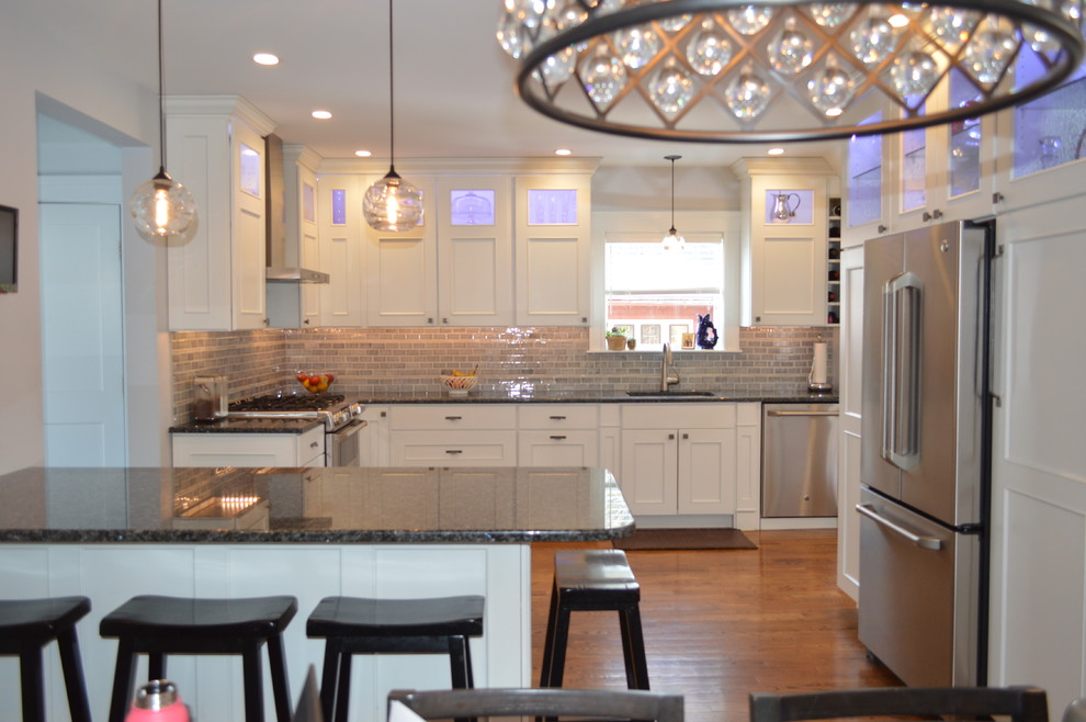 Example of a mid-sized transitional l-shaped medium tone wood floor eat-in kitchen design in Boston with an undermount sink, recessed-panel cabinets, white cabinets, granite countertops, gray backsplash, cement tile backsplash, stainless steel appliances, a peninsula and blue countertops