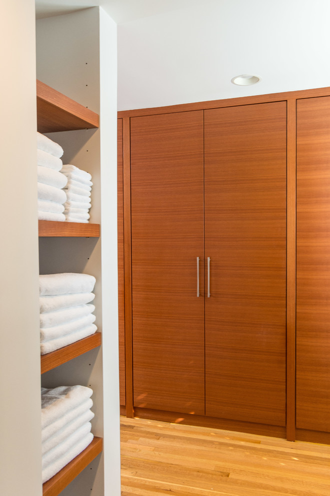 Photo of a mid-sized contemporary gender-neutral dressing room in Indianapolis with flat-panel cabinets, medium wood cabinets, light hardwood floors and brown floor.