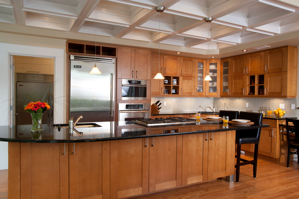 Example of a large transitional l-shaped medium tone wood floor eat-in kitchen design in Calgary with an undermount sink, shaker cabinets, medium tone wood cabinets, granite countertops, gray backsplash, glass tile backsplash, stainless steel appliances and an island