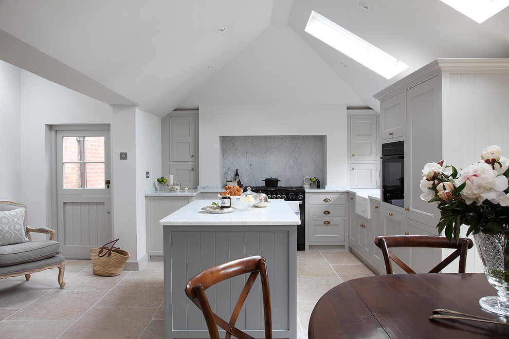 Design ideas for a country l-shaped eat-in kitchen in Surrey with a farmhouse sink, shaker cabinets, grey cabinets, grey splashback, stone slab splashback, black appliances and with island.