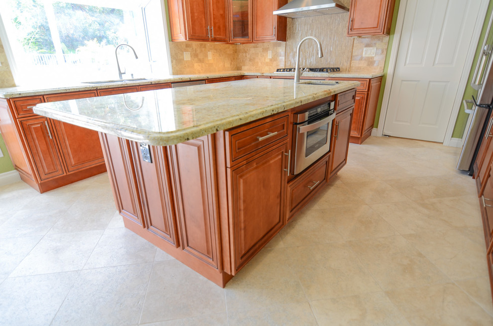 This is an example of a large traditional u-shaped open plan kitchen in Tampa with an undermount sink, raised-panel cabinets, light wood cabinets, granite benchtops, beige splashback, stone tile splashback, stainless steel appliances, travertine floors and with island.