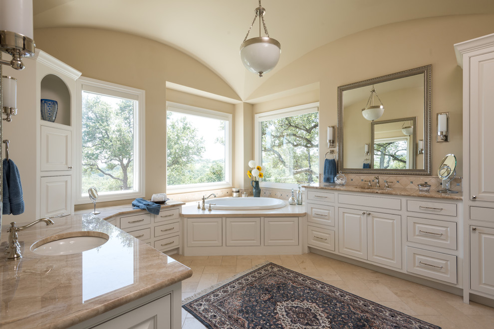 Design ideas for a large mediterranean master bathroom in Austin with raised-panel cabinets, white cabinets, a drop-in tub, beige tile, ceramic tile, beige walls, porcelain floors, an undermount sink, granite benchtops, beige floor and beige benchtops.