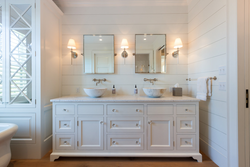 This is an example of a large beach style master bathroom in Boston with a vessel sink, recessed-panel cabinets, white cabinets, marble benchtops, white walls and medium hardwood floors.