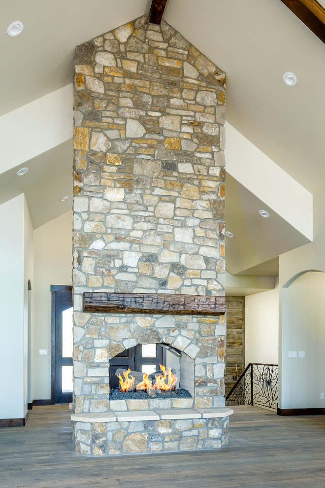 This is an example of a mid-sized country open concept living room in Denver with beige walls, dark hardwood floors, a two-sided fireplace and a stone fireplace surround.