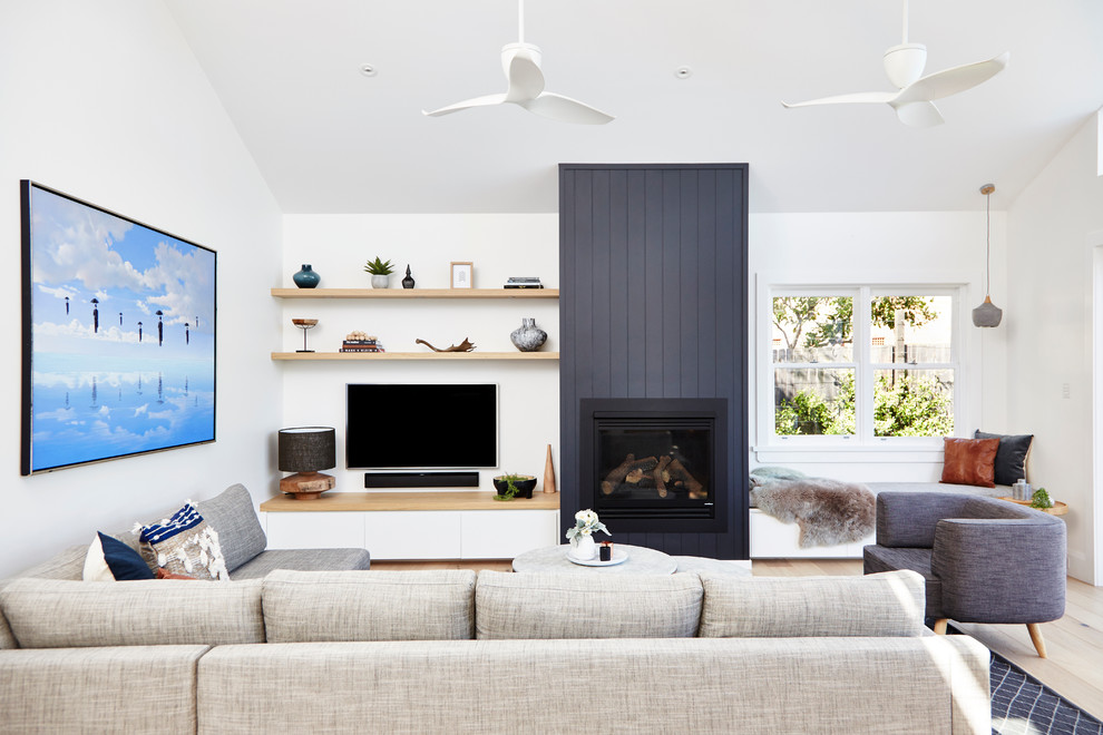 This is an example of a contemporary living room in Sydney with white walls, light hardwood floors, a wood stove, a wood fireplace surround and a wall-mounted tv.