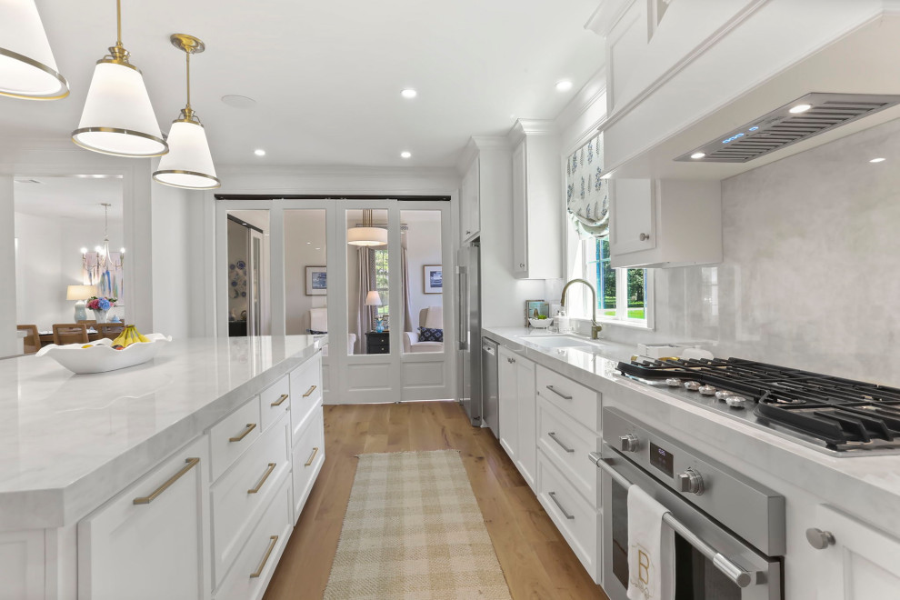 Inspiration for a large transitional l-shaped light wood floor and brown floor open concept kitchen remodel in New Orleans with an undermount sink, shaker cabinets, white cabinets, quartz countertops, white backsplash, quartz backsplash, stainless steel appliances, an island and white countertops