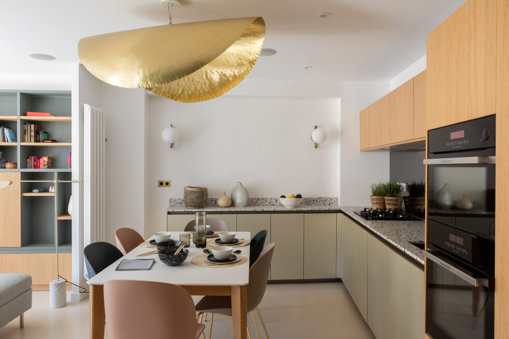 This is an example of a mid-sized contemporary l-shaped open plan kitchen in Paris with an undermount sink, beaded inset cabinets, light wood cabinets, terrazzo benchtops, metallic splashback, mirror splashback, panelled appliances, concrete floors and beige floor.
