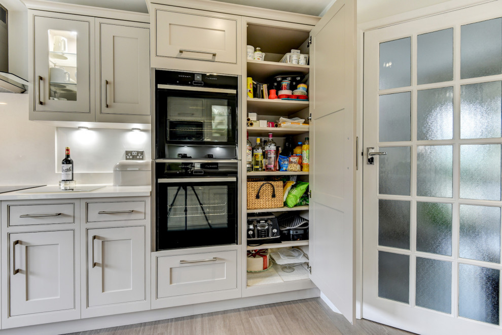 Design ideas for a large traditional grey and white galley enclosed kitchen in Sussex with a submerged sink, shaker cabinets, beige cabinets, quartz worktops, white splashback, black appliances, vinyl flooring, no island, brown floors, white worktops and feature lighting.