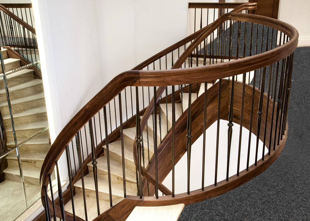 Diseño de escalera curva clásica grande con escalones de mármol, contrahuellas de madera y barandilla de varios materiales