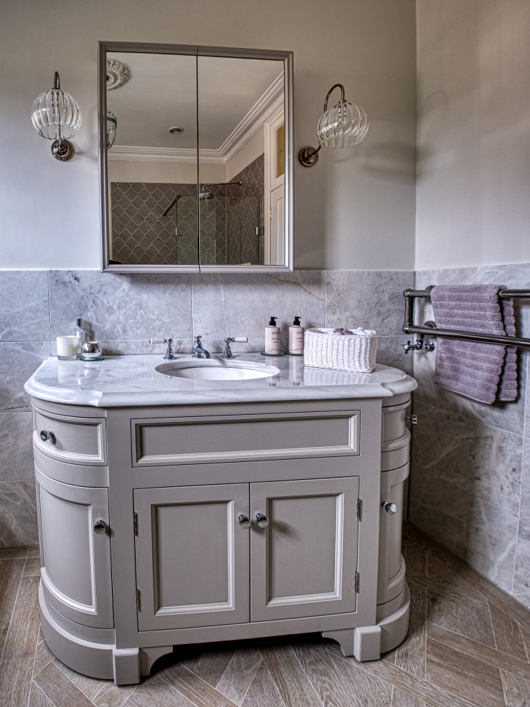 Photo of a large classic grey and cream bathroom in Surrey with shaker cabinets, beige cabinets, a claw-foot bath, a walk-in shower, a one-piece toilet, grey tiles, marble tiles, grey walls, porcelain flooring, a built-in sink, marble worktops, beige floors, an open shower, white worktops, a dado rail, a single sink and a freestanding vanity unit.