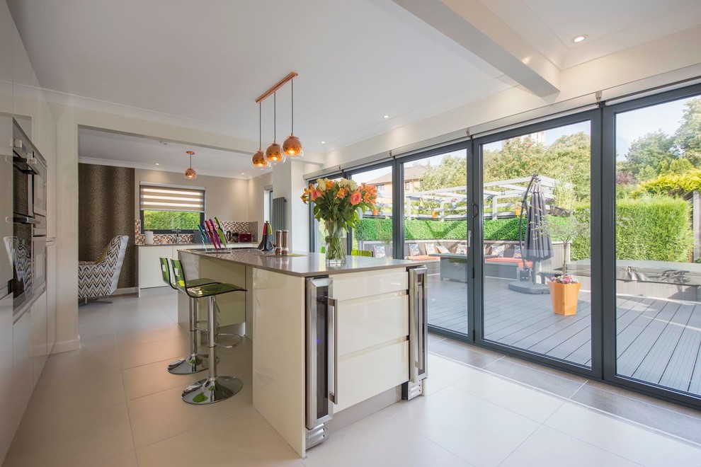 Contemporary single-wall kitchen with flat-panel cabinets, beige cabinets, stainless steel appliances, an island and white floors.