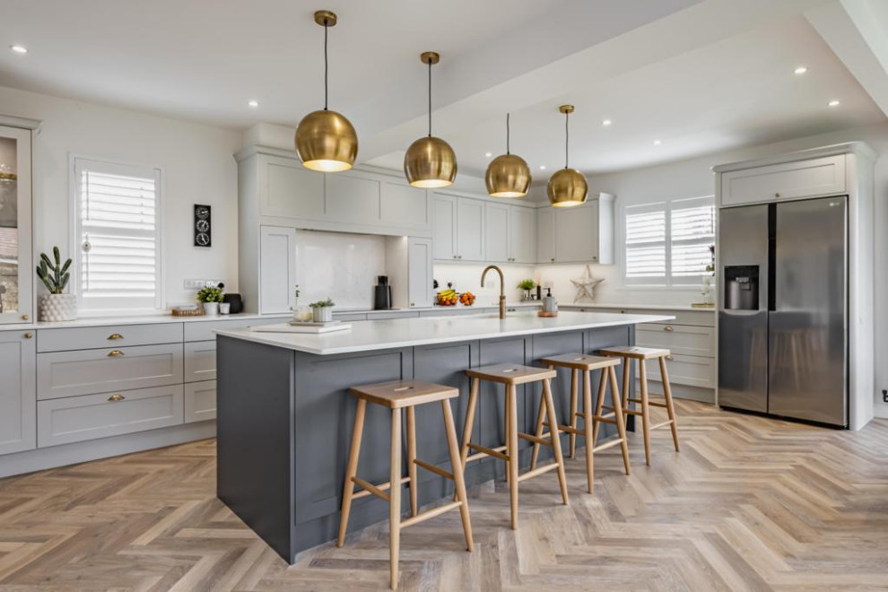 Photo of a large modern l-shaped eat-in kitchen in Other with an undermount sink, shaker cabinets, grey cabinets, quartzite benchtops, white splashback, stainless steel appliances, with island, brown floor and white benchtop.