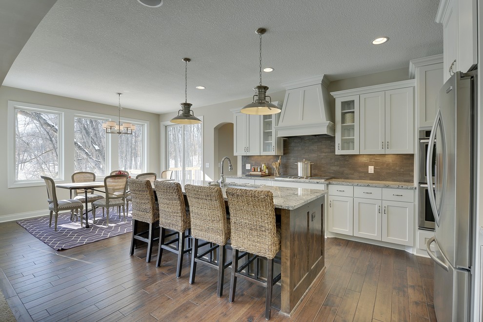 This is an example of a large transitional l-shaped eat-in kitchen in Minneapolis with an undermount sink, shaker cabinets, white cabinets, grey splashback, subway tile splashback, stainless steel appliances, dark hardwood floors and with island.