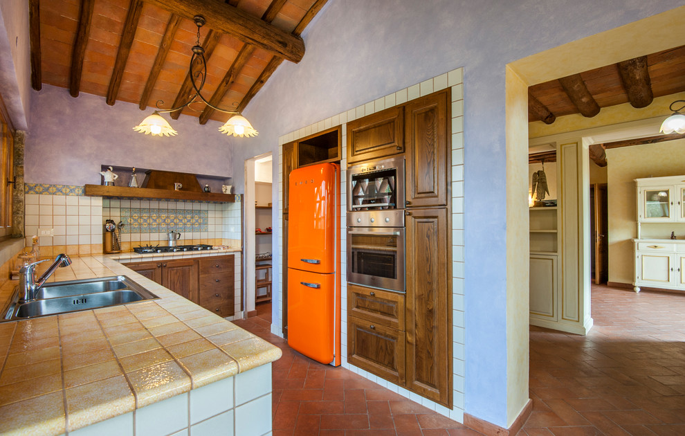 Photo of a mediterranean u-shaped kitchen in Florence with a drop-in sink, raised-panel cabinets, dark wood cabinets, multi-coloured splashback, coloured appliances, brick floors, no island, red floor and yellow benchtop.