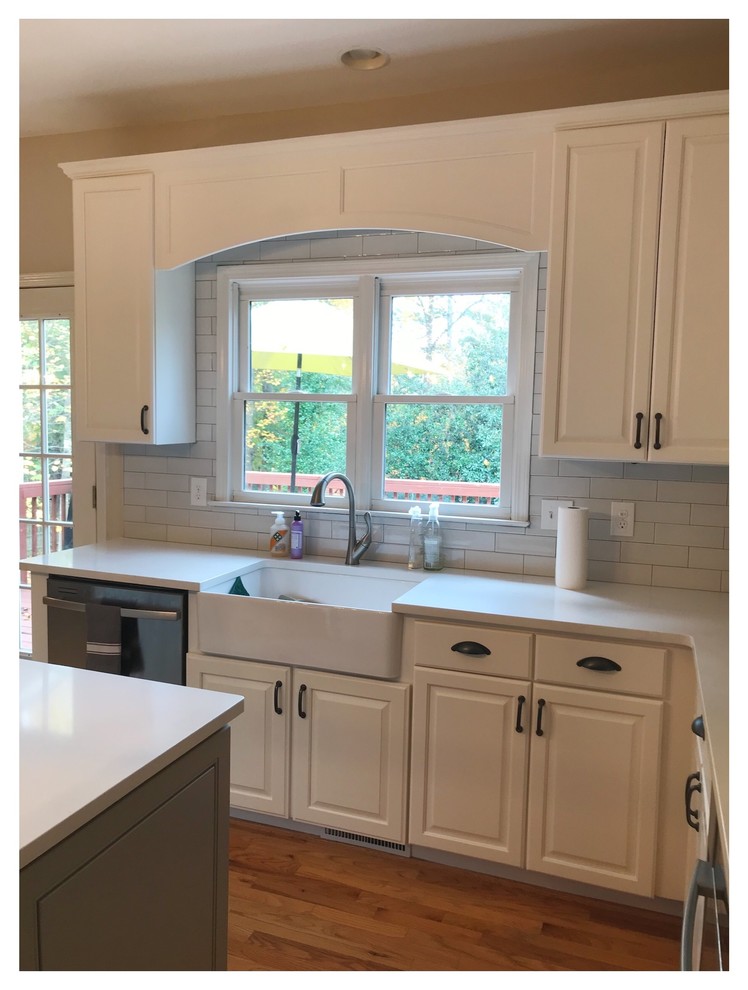 Design ideas for a mid-sized country u-shaped eat-in kitchen in Atlanta with a farmhouse sink, shaker cabinets, white cabinets, quartz benchtops, white splashback, subway tile splashback, stainless steel appliances, light hardwood floors, with island and brown floor.