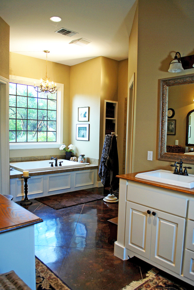 This is an example of a traditional bathroom in Austin with a drop-in sink, raised-panel cabinets, white cabinets, wood benchtops, a drop-in tub and brown tile.