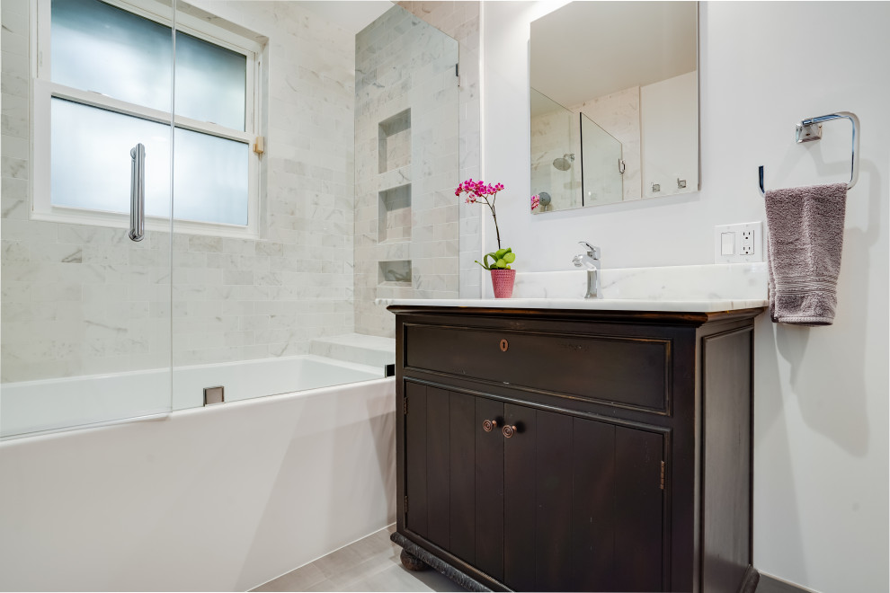 Mid-sized transitional master bathroom in San Francisco with furniture-like cabinets, brown cabinets, an alcove tub, a shower/bathtub combo, gray tile, marble, grey walls, porcelain floors, an undermount sink, marble benchtops, grey floor, a hinged shower door, white benchtops, a niche, a single vanity and a freestanding vanity.