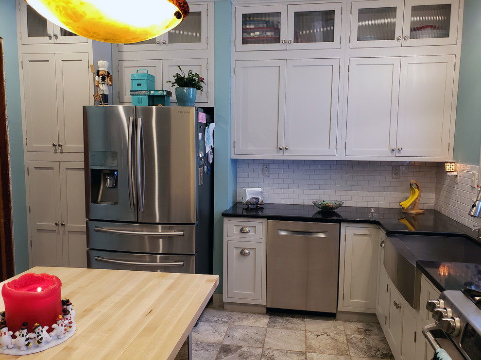 Inspiration for a large transitional u-shaped ceramic tile and beige floor kitchen pantry remodel with a farmhouse sink, recessed-panel cabinets, gray cabinets, quartz countertops, white backsplash, subway tile backsplash, stainless steel appliances, an island and black countertops