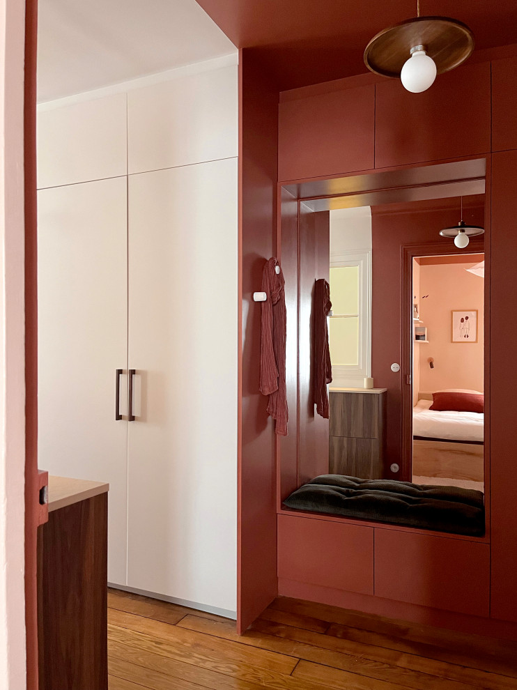 Exempel på en liten klassisk foajé, med röda väggar, ljust trägolv, en röd dörr och brunt golv