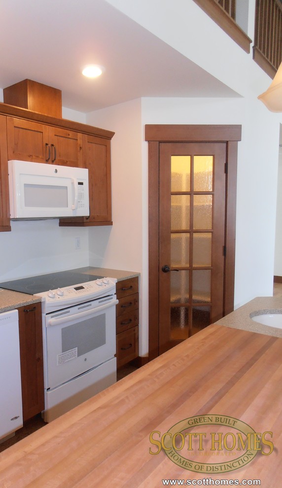 Photo of a mid-sized arts and crafts l-shaped open plan kitchen in Seattle with a farmhouse sink, shaker cabinets, medium wood cabinets, white appliances, cork floors and with island.
