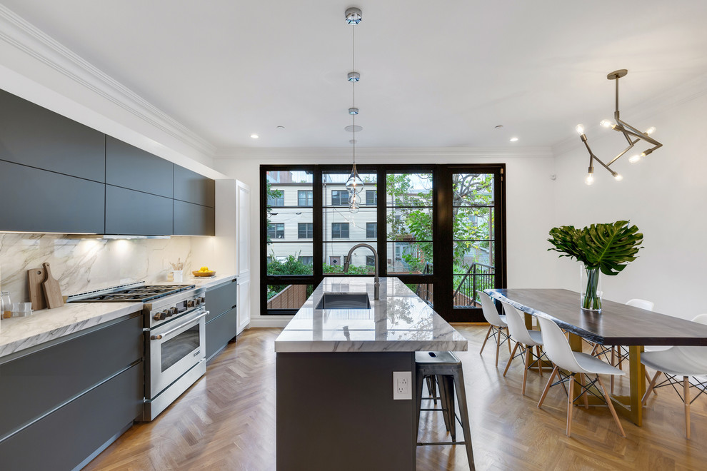This is an example of a transitional galley eat-in kitchen in New York with an undermount sink, flat-panel cabinets, black cabinets, marble benchtops, medium hardwood floors, with island, white splashback, stone slab splashback, stainless steel appliances, brown floor and white benchtop.