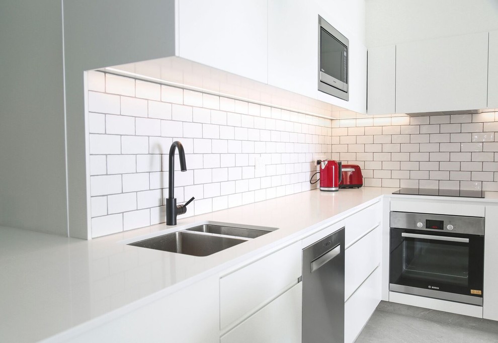 Design ideas for a small contemporary l-shaped eat-in kitchen in Sunshine Coast with a drop-in sink, recessed-panel cabinets, white cabinets, quartz benchtops, white splashback, subway tile splashback, stainless steel appliances, porcelain floors, no island, beige floor and white benchtop.