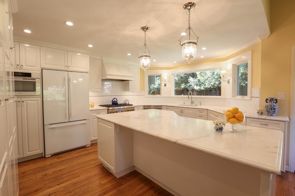 Example of a mid-sized transitional u-shaped light wood floor enclosed kitchen design in San Francisco with an undermount sink, beaded inset cabinets, white cabinets, marble countertops, white backsplash, subway tile backsplash, white appliances and an island