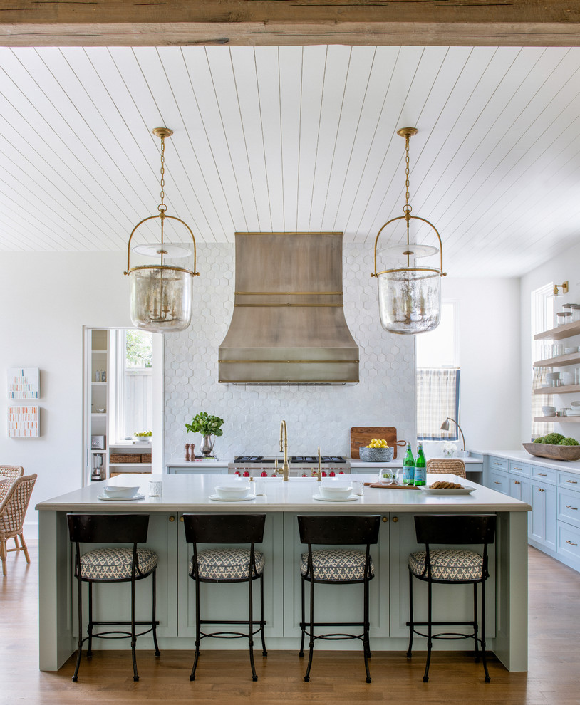 Design ideas for a beach style kitchen in Dallas with shaker cabinets, blue cabinets, white splashback, stainless steel appliances, medium hardwood floors, with island and white benchtop.