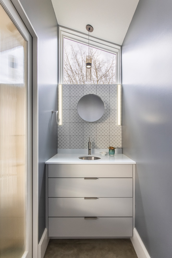 This is an example of a small contemporary powder room in Portland with flat-panel cabinets, grey cabinets, white tile, porcelain tile, grey walls, concrete floors, an undermount sink, engineered quartz benchtops, white benchtops and grey floor.