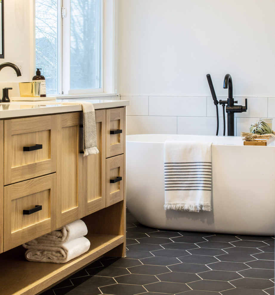 Inspiration for a mid-sized country master bathroom in Seattle with shaker cabinets, light wood cabinets, a freestanding tub, a corner shower, a one-piece toilet, white tile, subway tile, white walls, porcelain floors, an undermount sink, black floor, a hinged shower door, white benchtops and engineered quartz benchtops.