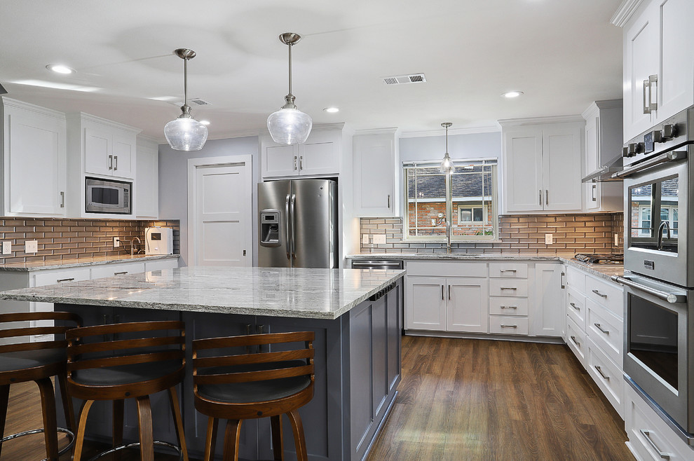 Inspiration for a large transitional u-shaped open plan kitchen in New Orleans with a single-bowl sink, shaker cabinets, white cabinets, granite benchtops, grey splashback, glass tile splashback, stainless steel appliances, vinyl floors, with island, brown floor and white benchtop.