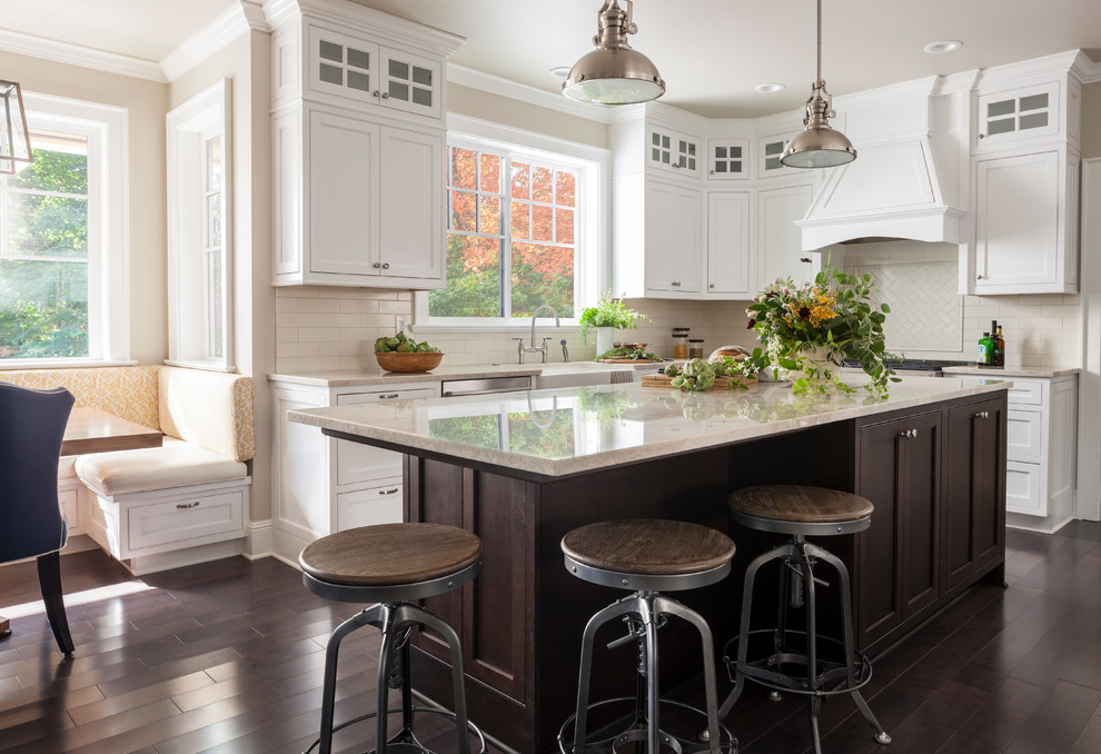 Photo of a mid-sized country l-shaped eat-in kitchen in Seattle with a farmhouse sink, shaker cabinets, white cabinets, white splashback, subway tile splashback, dark hardwood floors, with island, brown floor and stainless steel appliances.