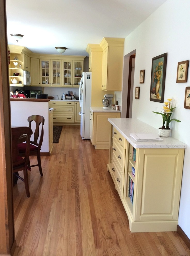 Inspiration for a mid-sized traditional l-shaped separate kitchen in Boston with raised-panel cabinets, yellow cabinets, solid surface benchtops and a peninsula.