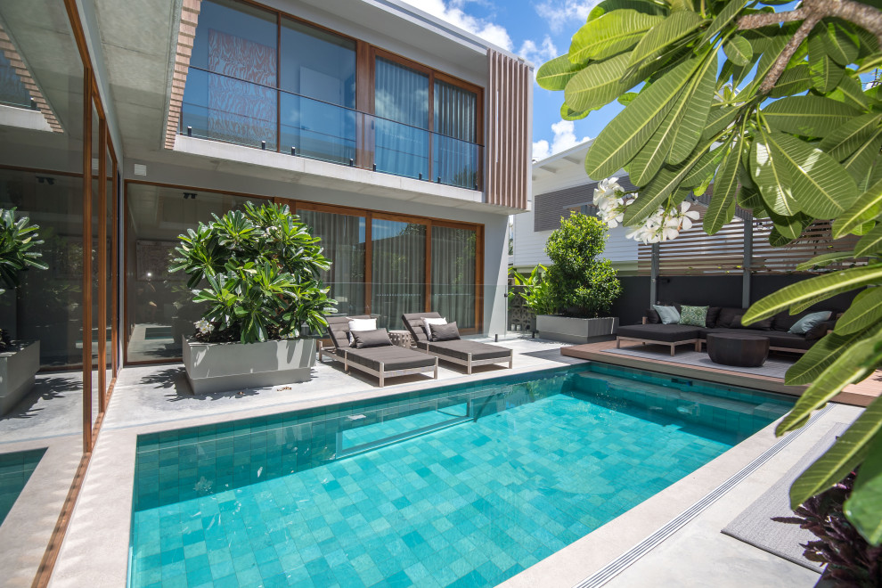 Ejemplo de piscina alargada exótica de tamaño medio rectangular en patio trasero con adoquines de hormigón