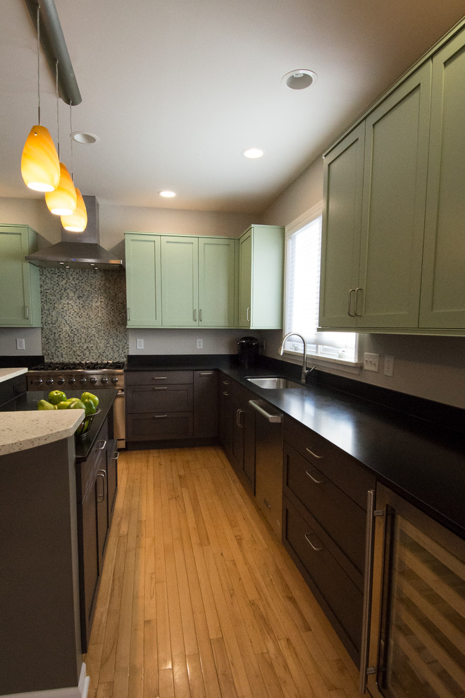 Photo of a mid-sized transitional u-shaped kitchen pantry in Detroit with an undermount sink, shaker cabinets, green cabinets, soapstone benchtops, green splashback, glass tile splashback, stainless steel appliances, light hardwood floors, with island, beige floor and black benchtop.