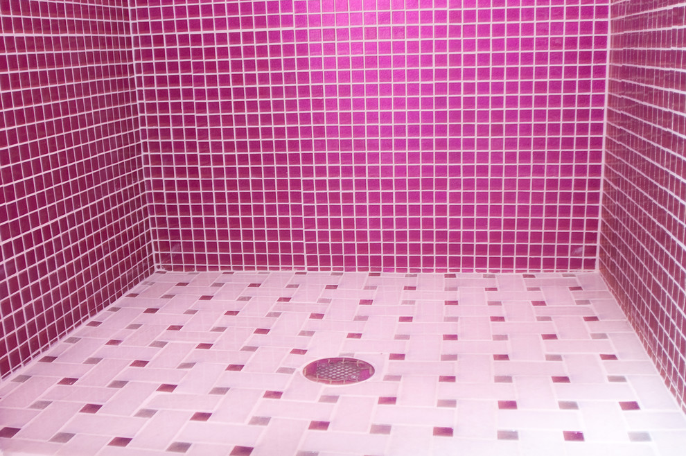Photo of a large modern bathroom in New York with open cabinets, a drop-in tub, a corner shower, a one-piece toilet, pink tile, mosaic tile, pink walls, ceramic floors, a wall-mount sink, glass benchtops and white floor.