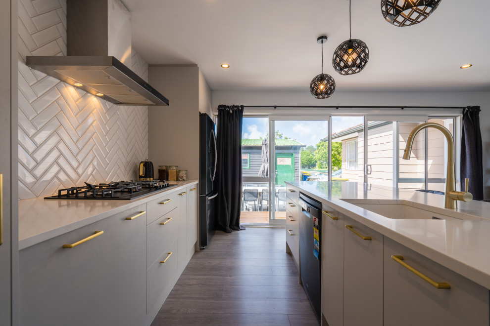 This is an example of a large contemporary galley kitchen/diner in Auckland with a submerged sink, grey cabinets, engineered stone countertops, white splashback, metro tiled splashback, black appliances, laminate floors, an island, grey floors and white worktops.