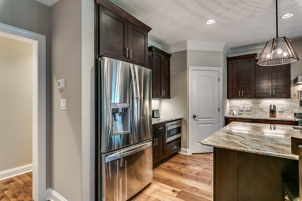 Inspiration for a large transitional l-shaped medium tone wood floor and brown floor open concept kitchen remodel with an undermount sink, shaker cabinets, dark wood cabinets, granite countertops, gray backsplash, stone tile backsplash, stainless steel appliances, an island and gray countertops