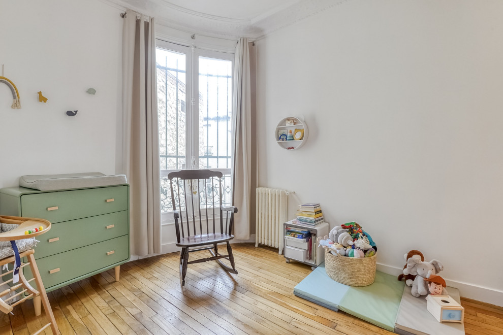 Idée de décoration pour une chambre de bébé neutre design de taille moyenne avec un mur blanc, parquet clair et un sol marron.