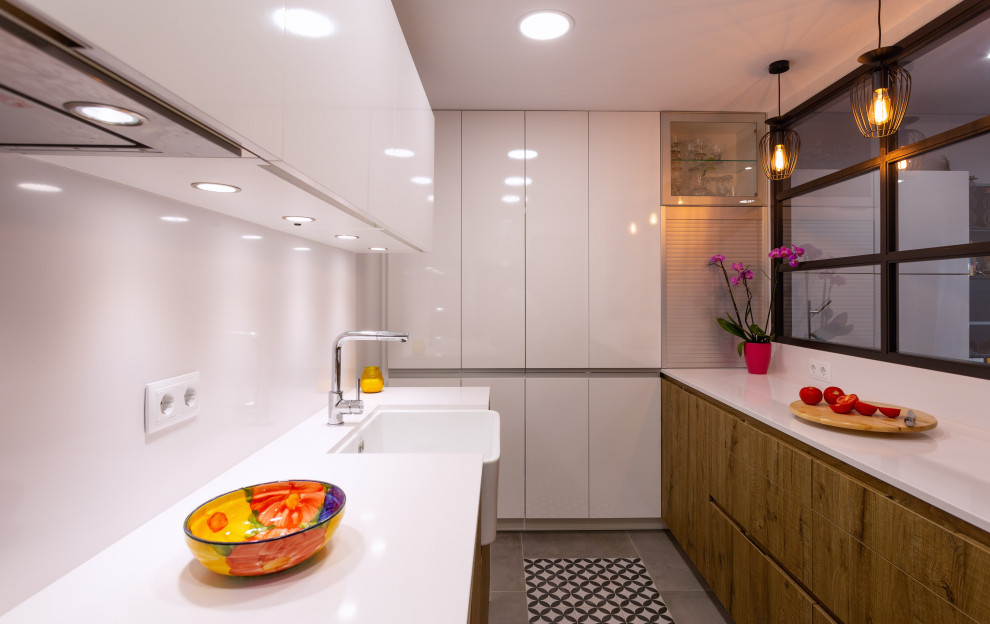 This is an example of a contemporary galley separate kitchen in Barcelona with a single-bowl sink, medium wood cabinets, white splashback, stainless steel appliances, no island, white benchtop and recessed.