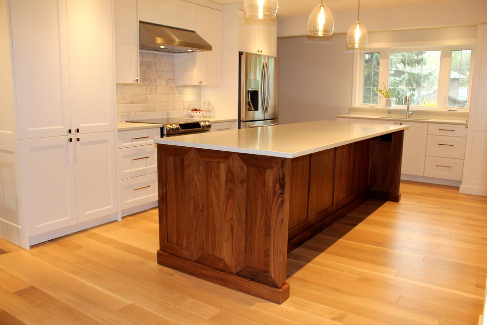 Example of a large transitional l-shaped light wood floor eat-in kitchen design with an undermount sink, shaker cabinets, white cabinets, quartz countertops, white backsplash, ceramic backsplash, stainless steel appliances and an island