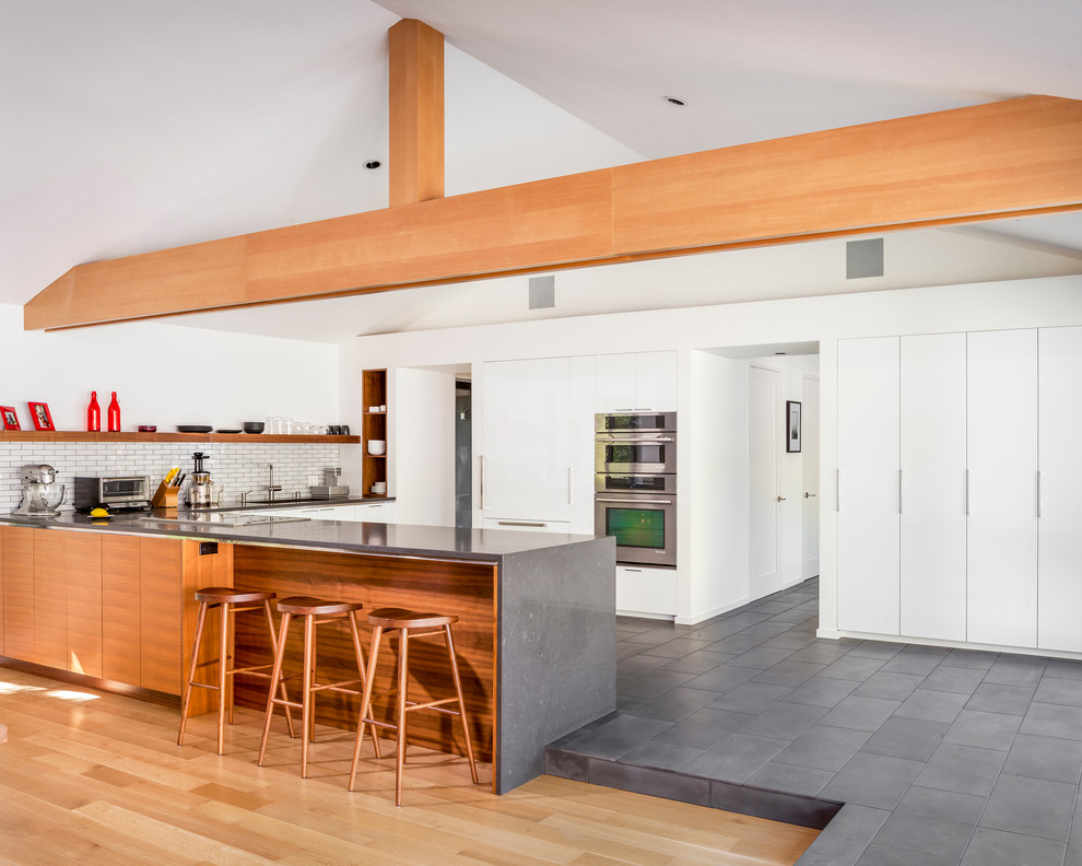 Photo of a scandinavian l-shaped eat-in kitchen in San Francisco with an undermount sink, flat-panel cabinets, white cabinets, quartzite benchtops, white splashback, subway tile splashback, stainless steel appliances, slate floors, a peninsula and grey floor.