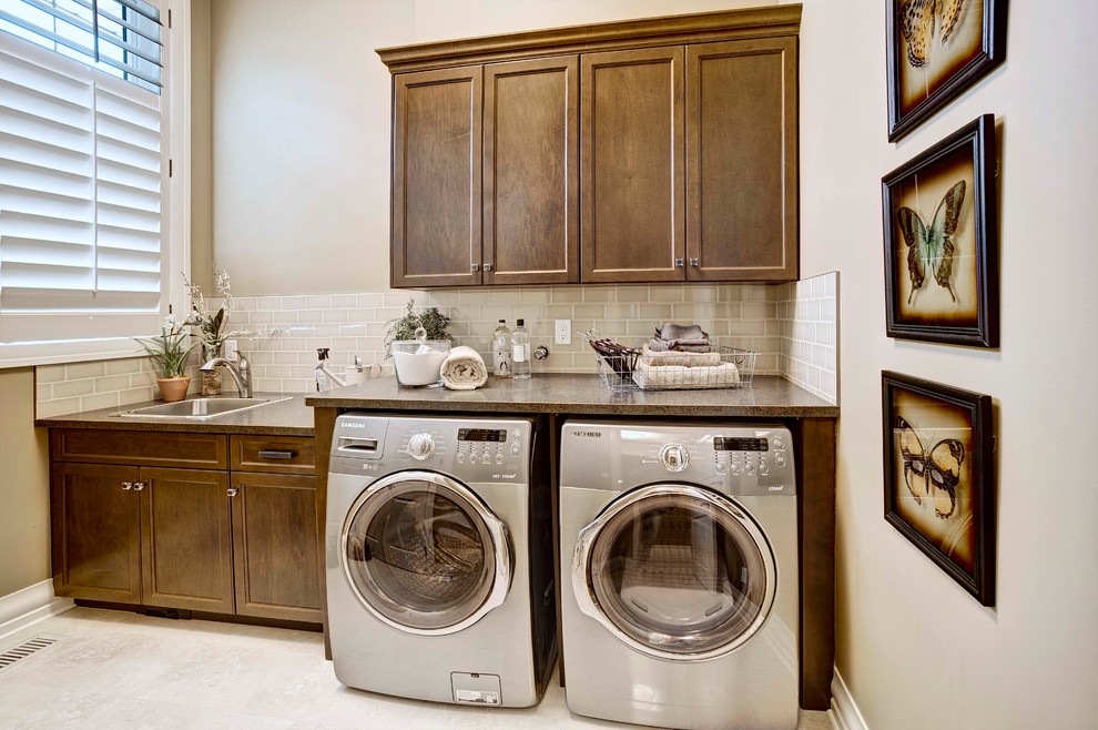 Inspiration for a traditional single-wall dedicated laundry room in Calgary with a drop-in sink, shaker cabinets, dark wood cabinets, beige walls, a side-by-side washer and dryer, white floor and grey benchtop.