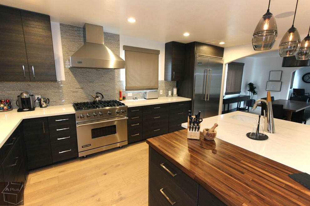 Large modern l-shaped eat-in kitchen in Orange County with a farmhouse sink, flat-panel cabinets, dark wood cabinets, quartzite benchtops, grey splashback, mosaic tile splashback, stainless steel appliances, light hardwood floors and with island.