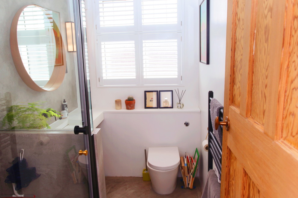This is an example of a small modern 3/4 bathroom in London with furniture-like cabinets, brown cabinets, an open shower, a wall-mount toilet, gray tile, cement tile, grey walls, concrete floors, a pedestal sink, terrazzo benchtops, grey floor, a hinged shower door and white benchtops.