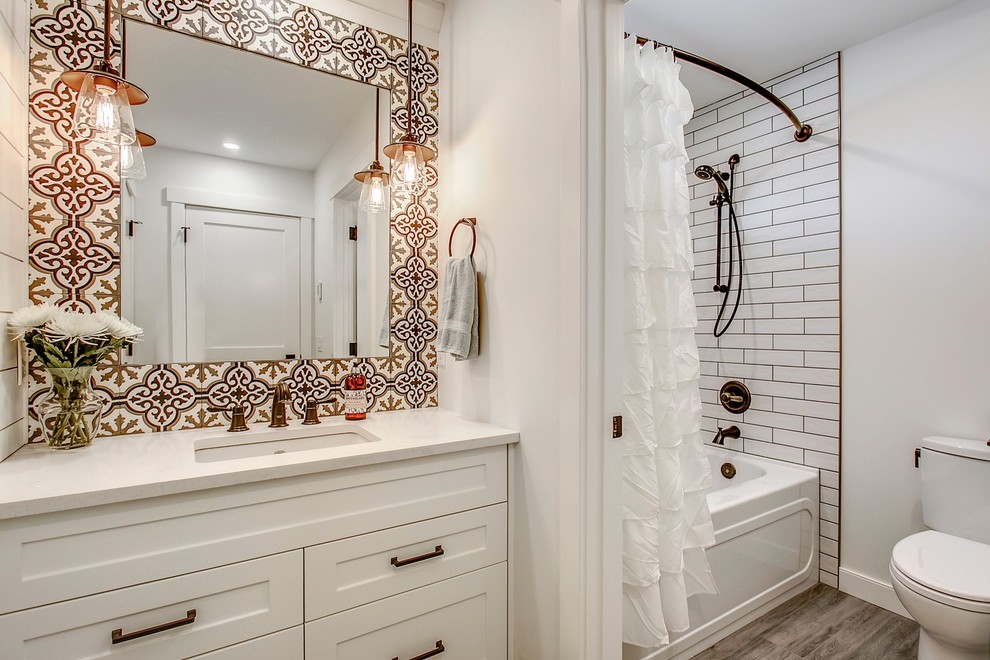 This is an example of a mid-sized transitional master bathroom in Calgary with shaker cabinets, white cabinets, an alcove tub, a two-piece toilet, white tile, cement tile, vinyl floors, an undermount sink, quartzite benchtops, grey floor, a shower/bathtub combo, white walls and a shower curtain.