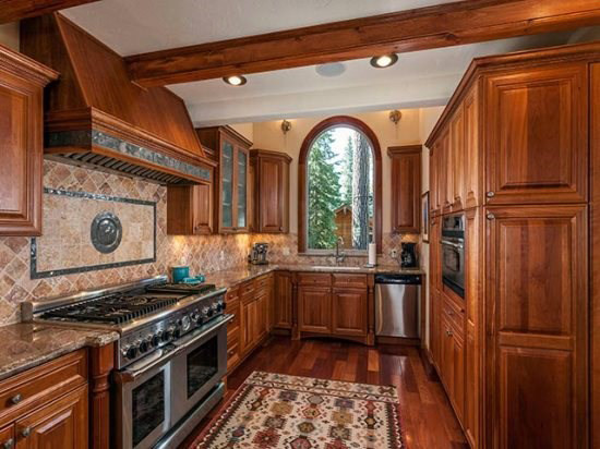 This is an example of a traditional galley kitchen pantry in Sacramento with an undermount sink, raised-panel cabinets, light wood cabinets, granite benchtops, orange splashback, terra-cotta splashback, stainless steel appliances, dark hardwood floors and with island.