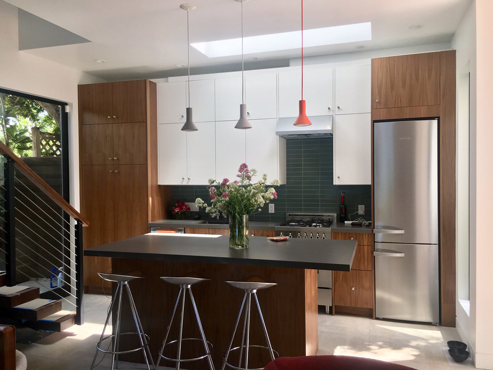Mid-sized contemporary single-wall eat-in kitchen in Los Angeles with an undermount sink, flat-panel cabinets, brown cabinets, solid surface benchtops, green splashback, ceramic splashback, stainless steel appliances, ceramic floors, with island, beige floor and black benchtop.