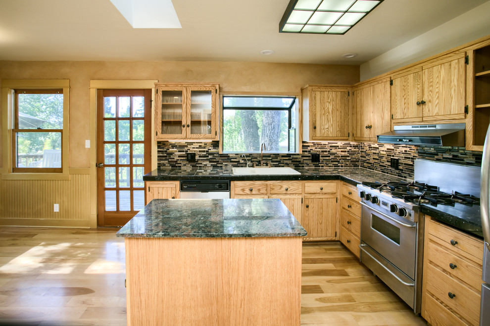 This is an example of a mid-sized arts and crafts l-shaped kitchen in Other with a drop-in sink, shaker cabinets, light wood cabinets, granite benchtops, brown splashback, matchstick tile splashback, stainless steel appliances, light hardwood floors, with island, brown floor and multi-coloured benchtop.