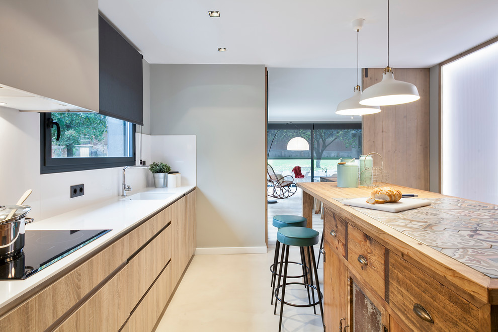 This is an example of a large contemporary galley separate kitchen in Barcelona with an integrated sink, flat-panel cabinets, light wood cabinets, tile benchtops, white splashback, stainless steel appliances, concrete floors and with island.